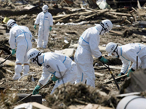 Японские полицейские в защитных костюмах ищут погибших от удара стихии в префектуре Фукусима.